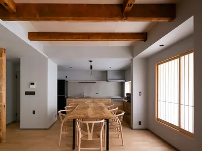 A modern kitchen with a wooden floor, a dining table, chairs, and appliances, lit by natural sunlight
