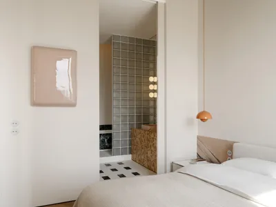 A bedroom with a bed, chair, and lamp, featuring a white color scheme and cozy atmosphere