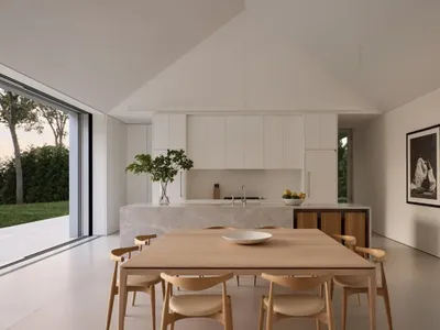 A modern kitchen with a wooden dining table, white cabinets, and natural light from a window, set with a bowl and oranges
