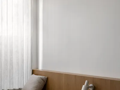 Cozy bedroom with a wooden bench, white walls, and a window with curtains, lit by a lamp