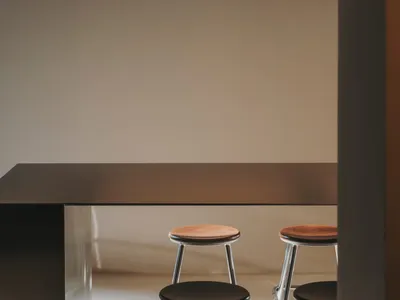 A modern kitchen with a wooden table and chairs, metal lighting, and a refrigerator in the background, set against a white wall and black countertop