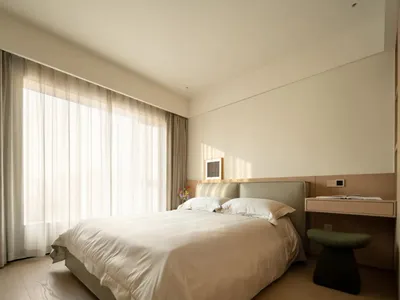 A calm bedroom with a bed, chair, and natural light from a window, featuring a white color scheme
