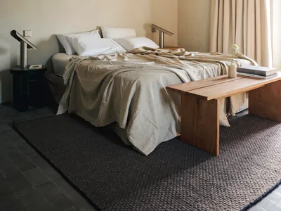 Cozy bedroom with a wooden floor, a white wall, and a dimly lit bed with a blanket and pillows