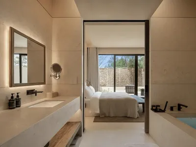 A modern minimalist bedroom with a bed, sink, and door, featuring predominantly white surfaces and a clean appearance