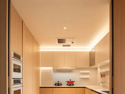 A modern kitchen with wooden cabinets, white countertops, a sink, oven, and microwave, lit by bright overhead lighting