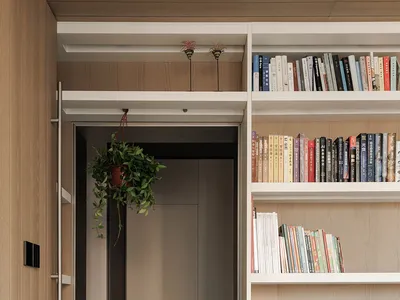 Cozy living area with a bookshelf filled with books, a potted plant, and a doorway, set against a neutral background