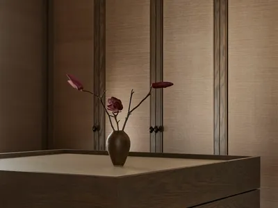 A cozy bedroom with a wooden dresser, a vase of flowers, and a bed in the background, creating a warm and inviting atmosphere