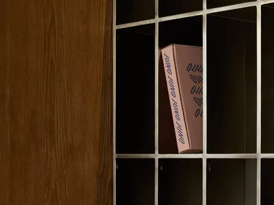 A cozy living space with a wooden cabinet, metal shelf, and a pink box on top, surrounded by books and a warm atmosphere