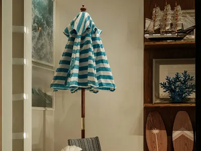 A modern living room with a blue and white striped umbrella hanging from the ceiling, a chair, table, and surfboard, with a warm and natural feel from the wood materials and well-lit atmosphere