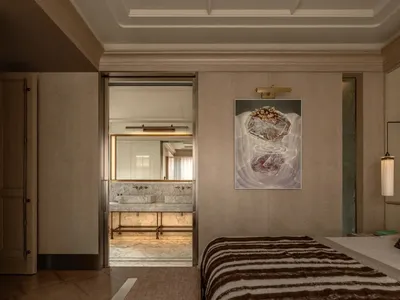 A well-lit bedroom with a bed, chair, and painting, featuring wood and fabric materials, creating a warm and inviting atmosphere