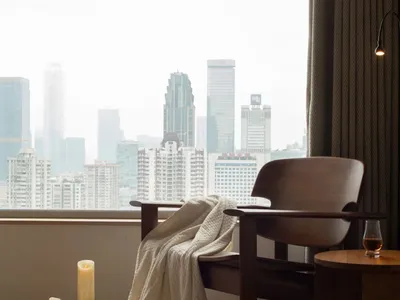 Cozy living room with a wooden chair near a window, a table in front, and a city view through the large window