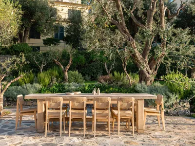 A wooden dining table and chairs set up on a patio surrounded by potted plants, ready for a meal, with a warm and inviting atmosphere
