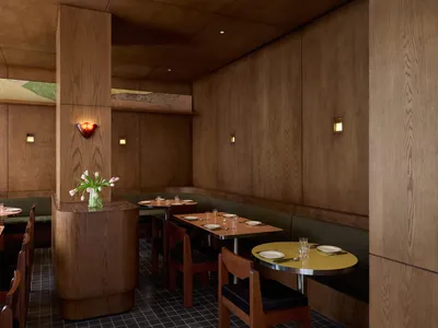 A warm and inviting restaurant interior with wooden tables, chairs, and decor, set with plates, wine glasses, and utensils, encouraging conversation and interaction among guests
