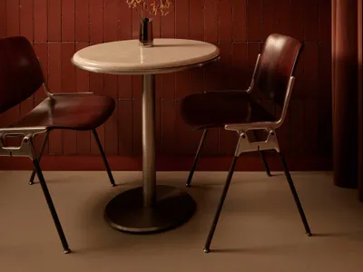 Dining area with a red brick wall, a dining table, and two chairs, surrounded by additional chairs and a vase with flowers