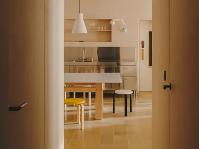 A modern kitchen with a wooden floor, dining table, chairs, and natural light from windows
