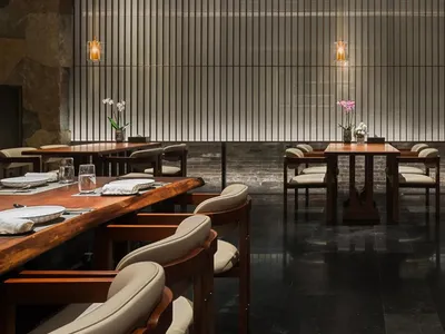 A well-lit dining space with multiple tables and chairs, set with wine glasses, vases, and other tableware, in a sophisticated atmosphere
