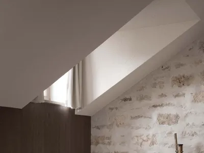 Small bathroom with a white bathtub, sink, and window, set against a stone wall and wooden floor in a dimly lit space