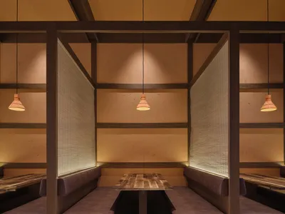 一間現代餐廳的木材內裝，餐廳區域有桌子和長凳，吧檯有計票台，低調的照明營造溫暖的氛圍