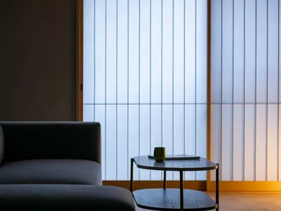 Cozy modern living room with a gray couch, a black table, and dim lighting, decorated with a cup and a vase, featuring wood and metal materials