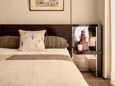 Cozy bedroom with a bed covered in a white blanket, a wooden headboard, and a picture frame on the wall, with a table and lamp nearby