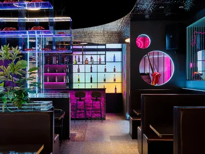 Modern bar and restaurant interior with black and white decor, featuring multiple chairs, dining tables, and a well-stocked bar with bottles and wine glasses