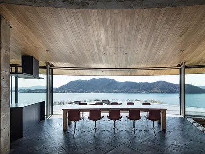 A large dining room with a wooden floor, a dining table, and chairs, offering a cozy and inviting atmosphere with a view of the water outside