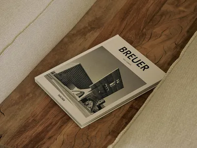 A modern hotel lobby with a white couch on a wooden floor, a magazine on top, and a sleek building in the background
