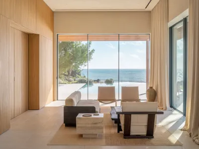 Coastal living room with a large window overlooking the ocean, featuring a couch, chair, and coffee table, with a modern style and neutral color palette