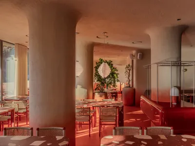 Cozy modern restaurant interior with red walls, wooden furniture, and potted plants, featuring soft warm lighting