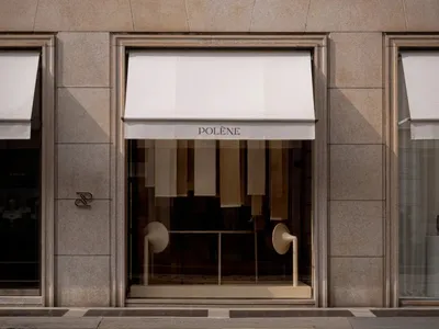 A classic storefront with a stone exterior, white awning, and window display featuring white curtains and a table, set against a bright and welcoming background