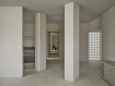 A bright and inviting kitchen and hallway with white walls, tile floors, and natural light from windows