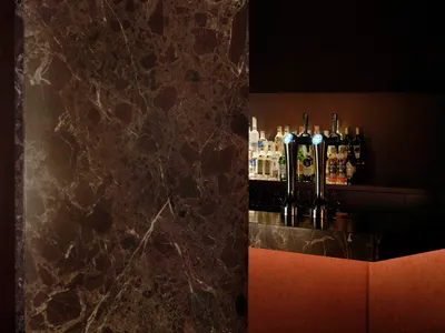 A modern bar with a marble countertop featuring various bottles arranged in a visually appealing way, set in a well-lit environment