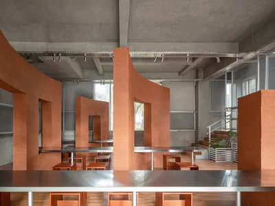 A modern restaurant with a large dining table and benches, surrounded by concrete walls and wooden accents, in a well-lit space