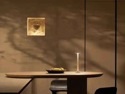 A dining area with a wooden table and chairs, set with a bowl of fruit, lit by a table lamp