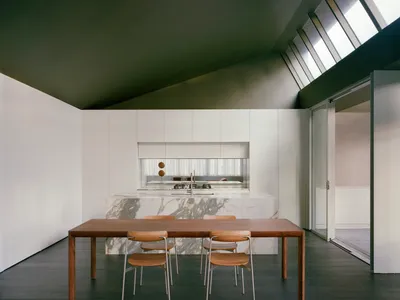 A modern kitchen with a wooden dining table and chairs, surrounded by a sink and oven, in a well-lit space with neutral colors and a focus on wood elements
