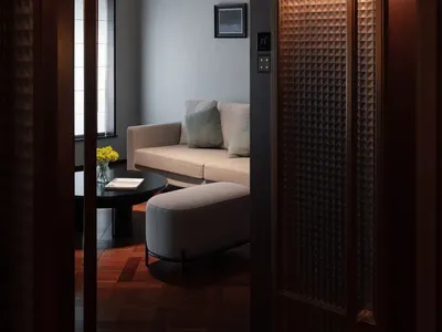 A well-lit living room with a grey couch, a chair, a coffee table, and decorative items, creating a warm and inviting space with wood and fabric materials
