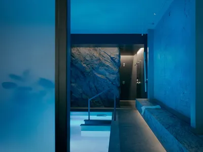 blue-toned bathroom with a large pool, bench, and shower, featuring a modern and luxurious design with marble or high-end tiles