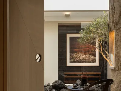 Cozy living space with a wooden door, a bench, a dining table, and a potted plant, set against a stone wall with a wooden floor and dim lighting