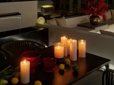 Cozy modern living room with a dining table, candles, and potted plants, illuminated by natural light through windows