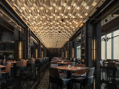 A modern restaurant with a semi-circular seating arrangement, wine glasses, and vases on tables, surrounded by a mix of black and brown colors and various materials, with soft and warm lighting