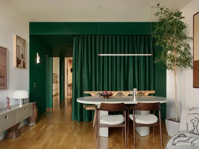 Dimly lit dining room with a green table and chairs, surrounded by a potted plant, in a modern style with a focus on comfort and functionality