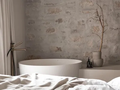 Cozy minimalist bedroom with a white bed and stone wall, featuring a bathtub and soft diffused lighting