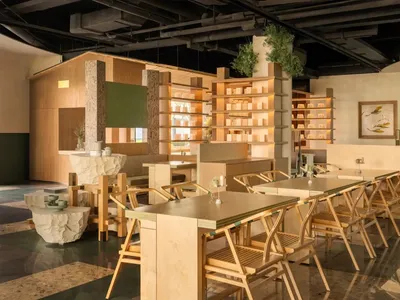 A modern restaurant interior with multiple tables, chairs, and potted plants, well-lit and welcoming