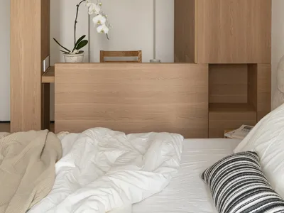 A cozy bedroom with a wooden floor, white walls, a bed, a desk, and a chair, creating a comfortable atmosphere