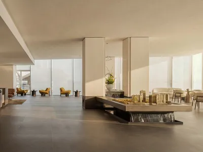 A large, open room with a modern design, natural light, and white finishes, featuring a couch, chairs, and a dining table