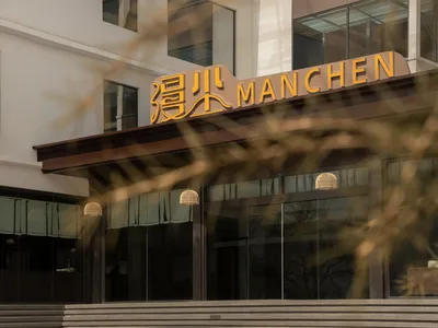 一座現代飯店建築，玻璃前面和黑框架，背後有外語招牌，從低角度拍攝，使用柔和和散射光源