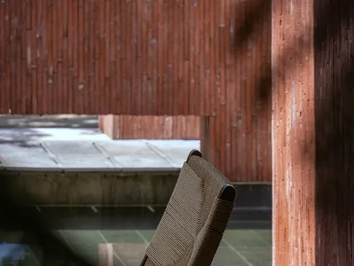 Cozy living space with a chair and couch, wooden floor, and brick wall, lit by natural sunlight