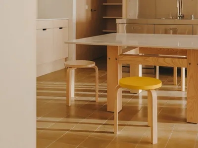 Modern kitchen with wooden floors and cabinets, featuring a sink, refrigerator, dining table, and chairs, with natural light and a warm atmosphere