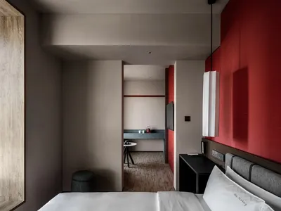 A warm and inviting hotel bedroom with a red-painted room, a black and white color scheme, and a bed positioned against a red wall, accompanied by a table and chair