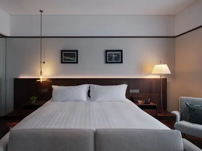 A well-lit bedroom with a large bed, wooden headboard, and nightstand, featuring a lamp and a picture above the bed
